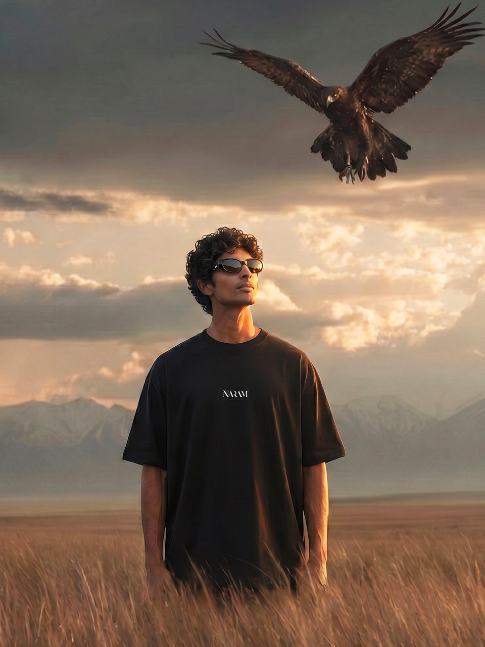 
Man wearing Naram black oversized tee with eagle flying above in golden field, Indian streetwear lifestyle shot